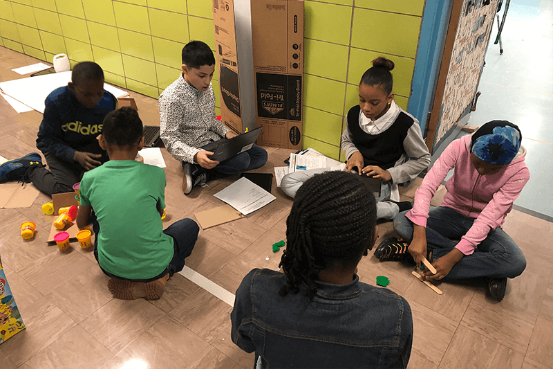 Children sit in a circle on the floor working on a project