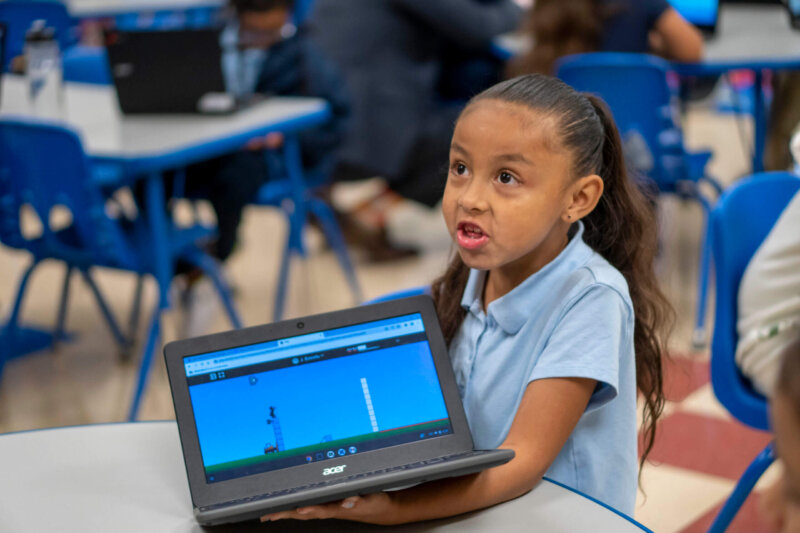 Young girl in blue shirt holds a laptop