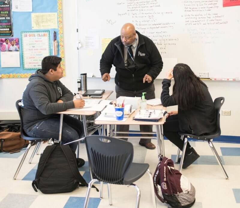 Teacher talks with two students at desks