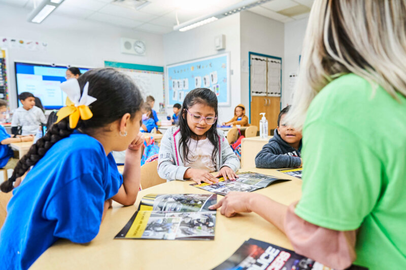 two students sit at a table with a teacher