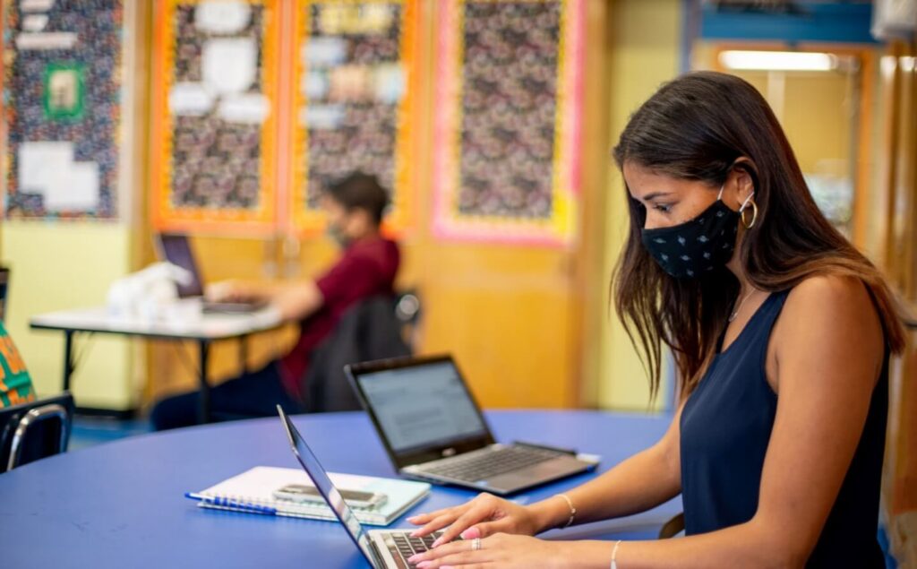 teacher wearing face mask works on laptop