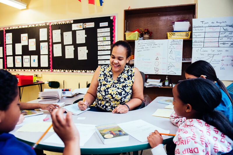 Teacher sits with students in a classroom