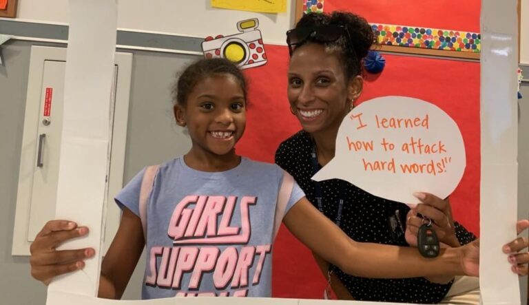 Student holds paper sign with adult standing behind her