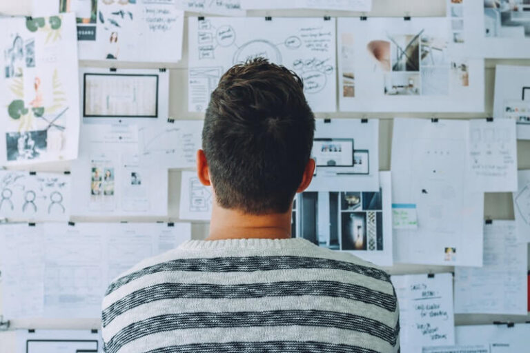 man wearing black and white striped shirt looks at wall covered in paper
