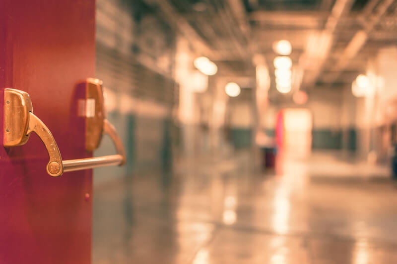 Red school door open to empty hallway