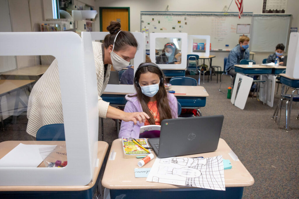 A fifth-grade teacher helps a student with a computer-based lesson in class.