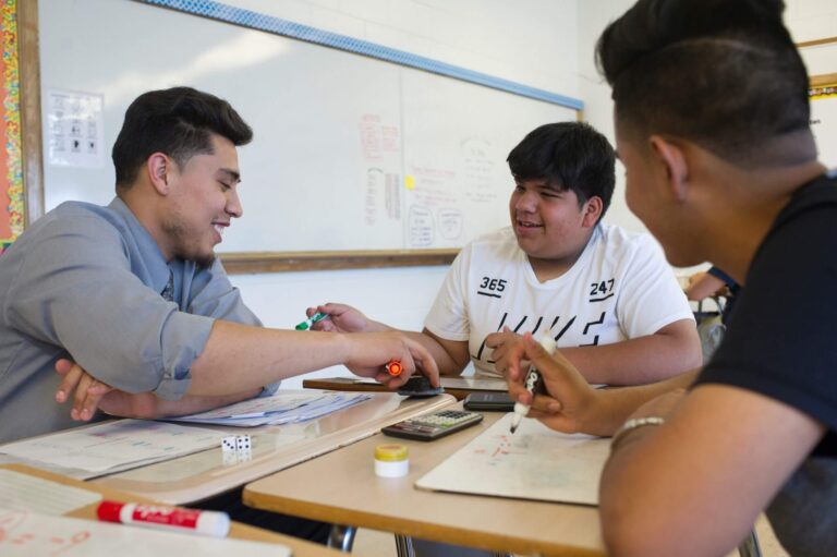 Teacher talks with two students at desks