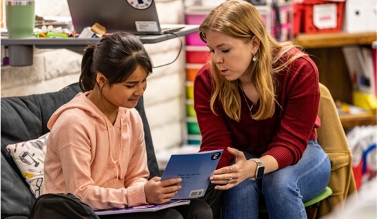 teacher sits with student in classroom