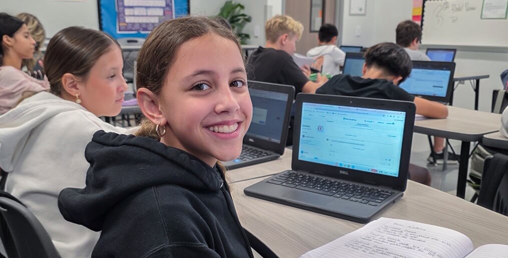 student smiles while sitting with laptop