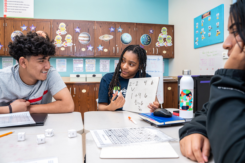 tutor holds whiteboard at table with students