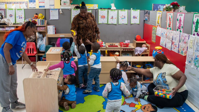 Children wearing blue vests in classroom with educators