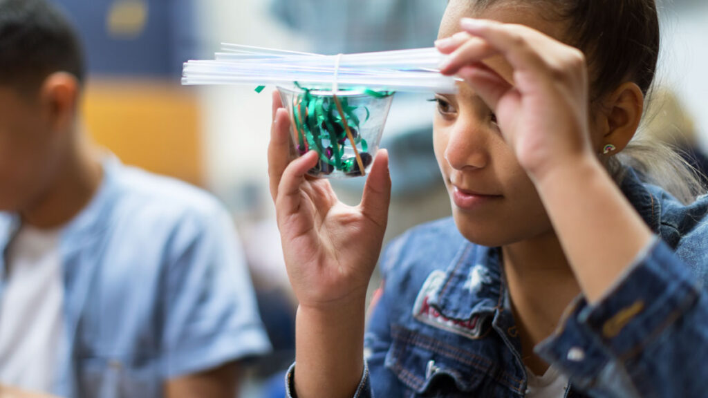 girl holds cup filled with string, tied to plastic straws