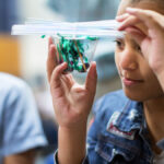 girl holds cup filled with string, tied to plastic straws