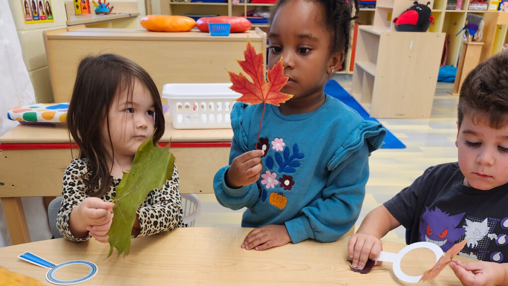 Three young children sit at table playing with leaves