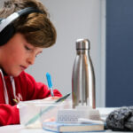 student in red sweatshirt with headphones on sits with laptop