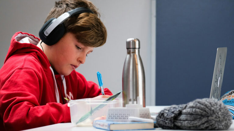 student in red sweatshirt with headphones on sits with laptop